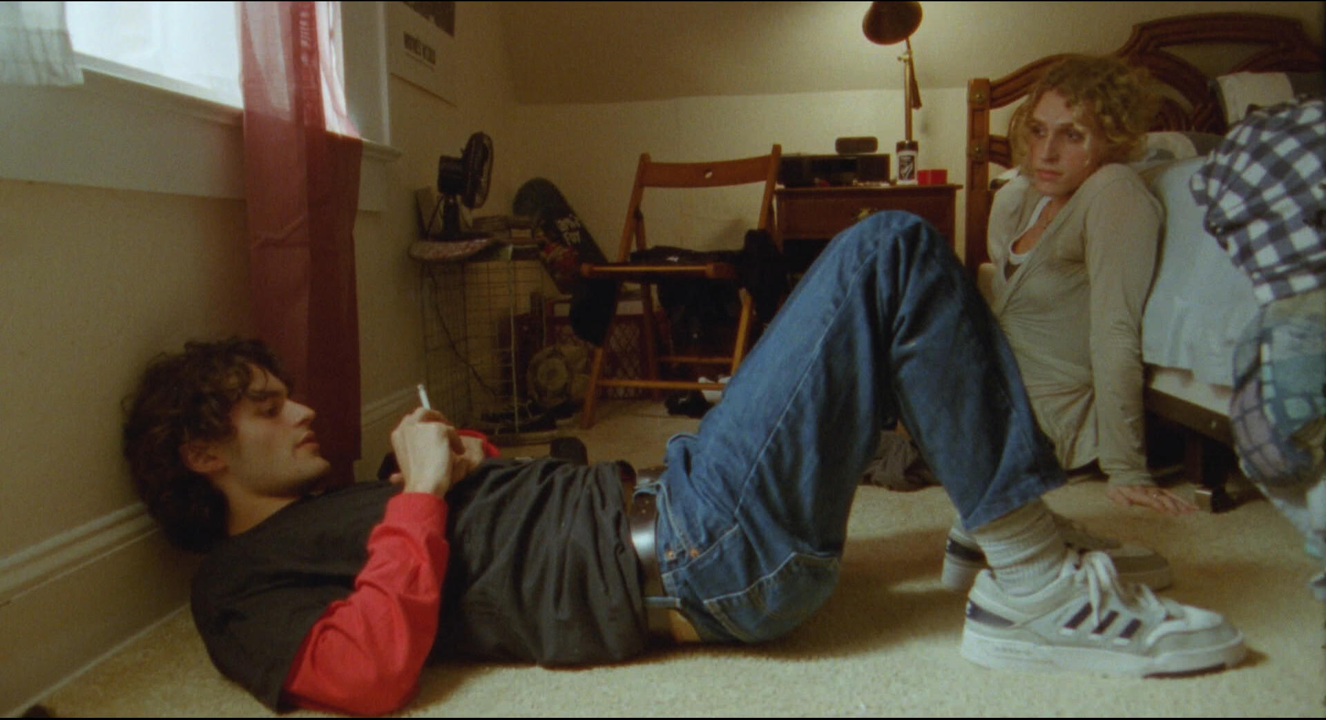 MP Still 4 Molly and Tom sit on the floor of tom's room. Tom is laying on the ground with a cigarette; Molly is sitting on the floor, leaning against the bed.